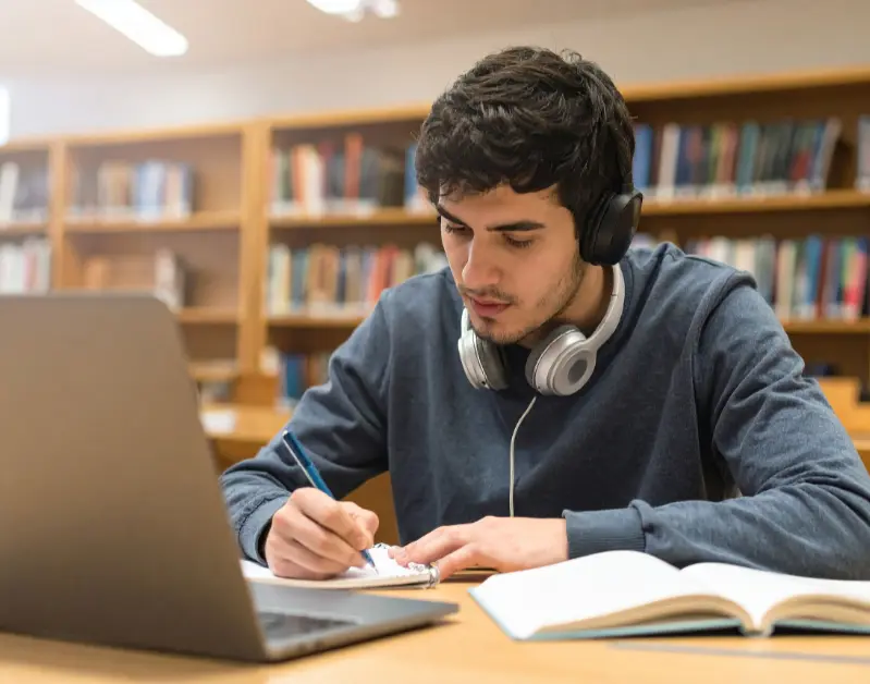 A student writing a thesis statement on a laptop for essay writing.